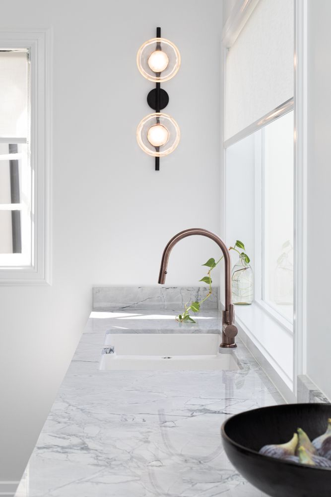 Stunning kitchen detail showcasing white marble countertop, unique vertical pendant lights, and a modern bronze tap against a crisp white backdrop.