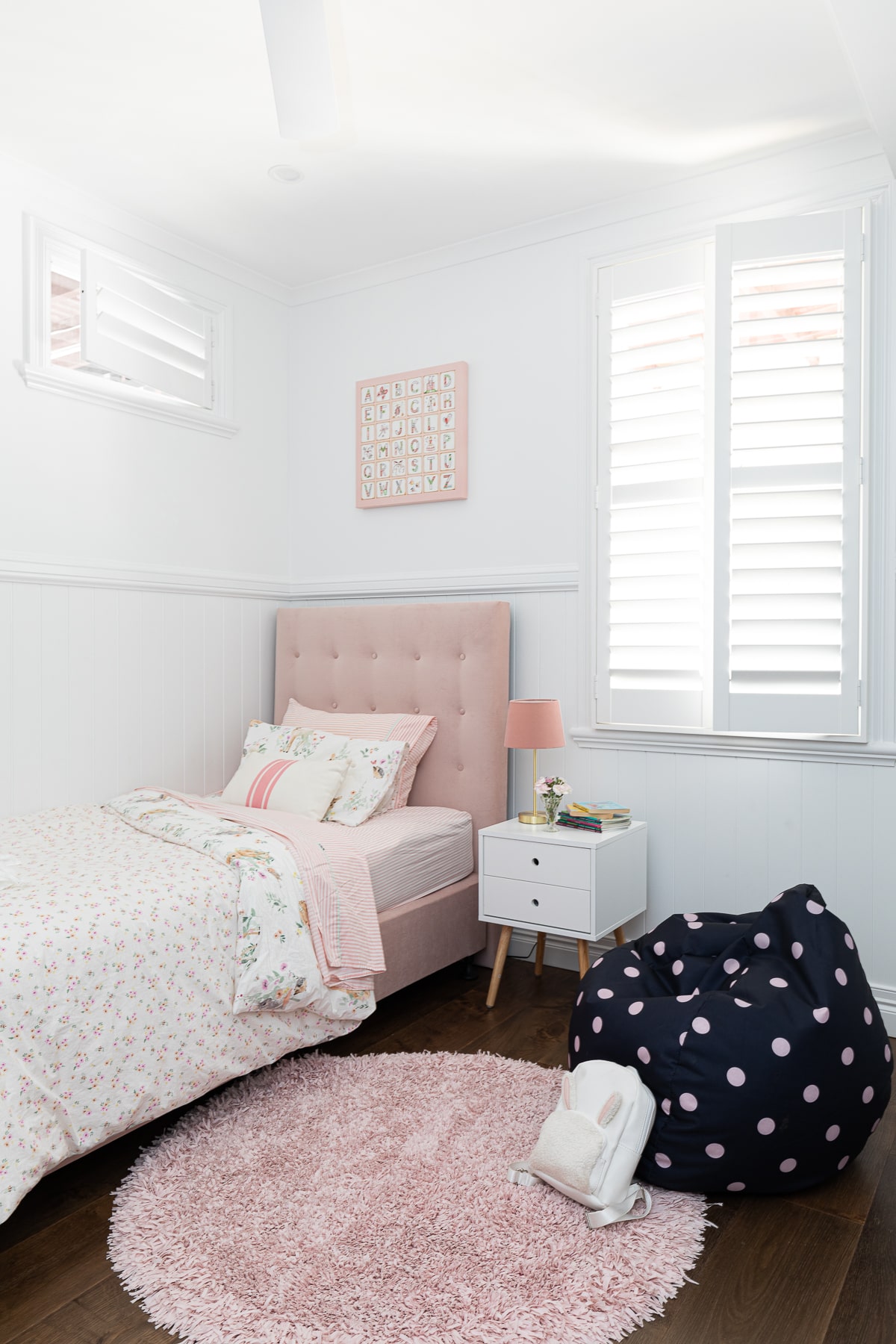 A cosy children's bedroom with a blush pink tufted bed, pastel bedding, a plush round rug, and playful polka dot bean bag, creating a whimsical space for rest and play.