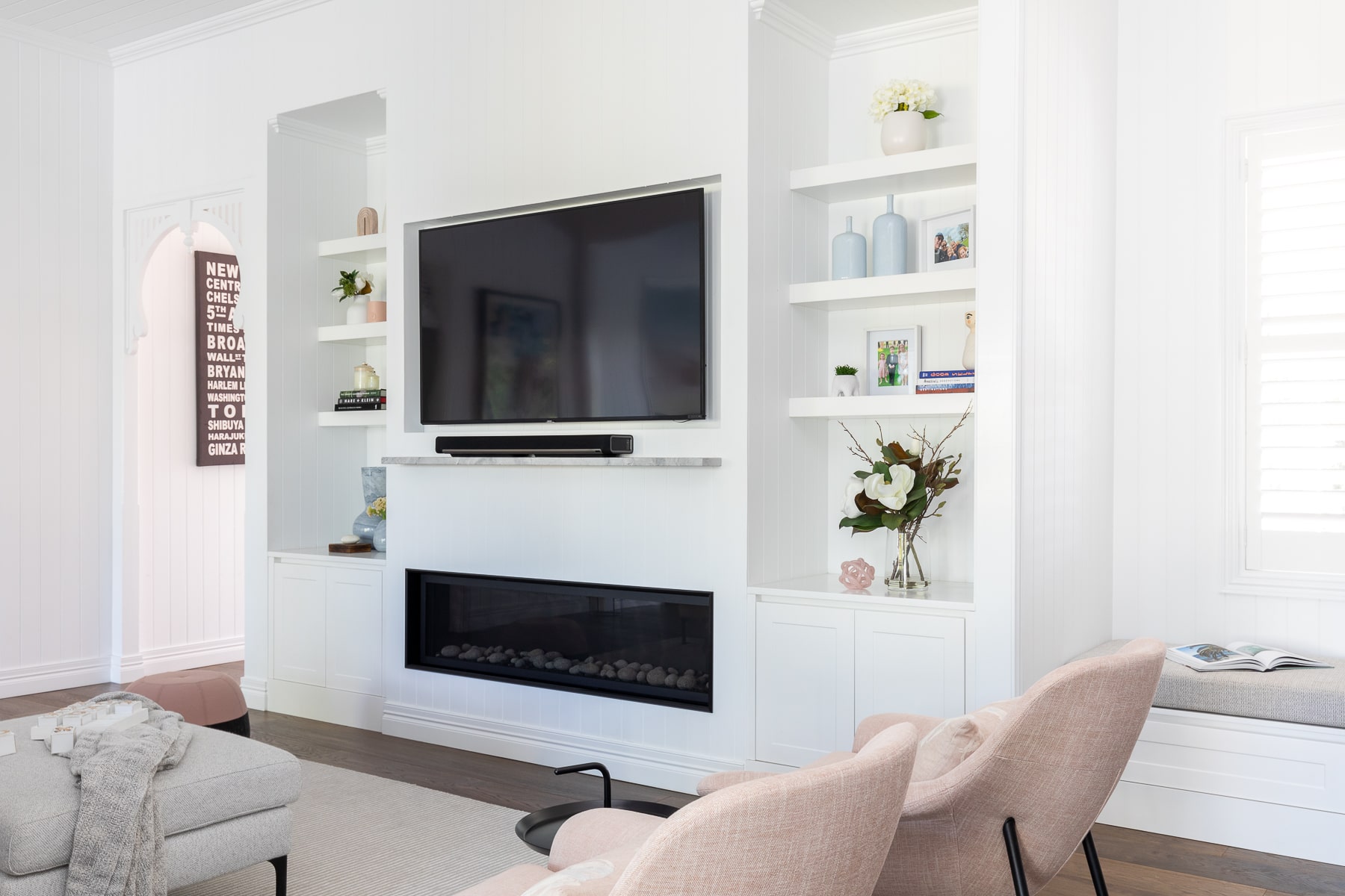 Contemporary living room showcases a wall-mounted TV above a sleek electric fireplace, with custom white shelving and elegant home decor accents.