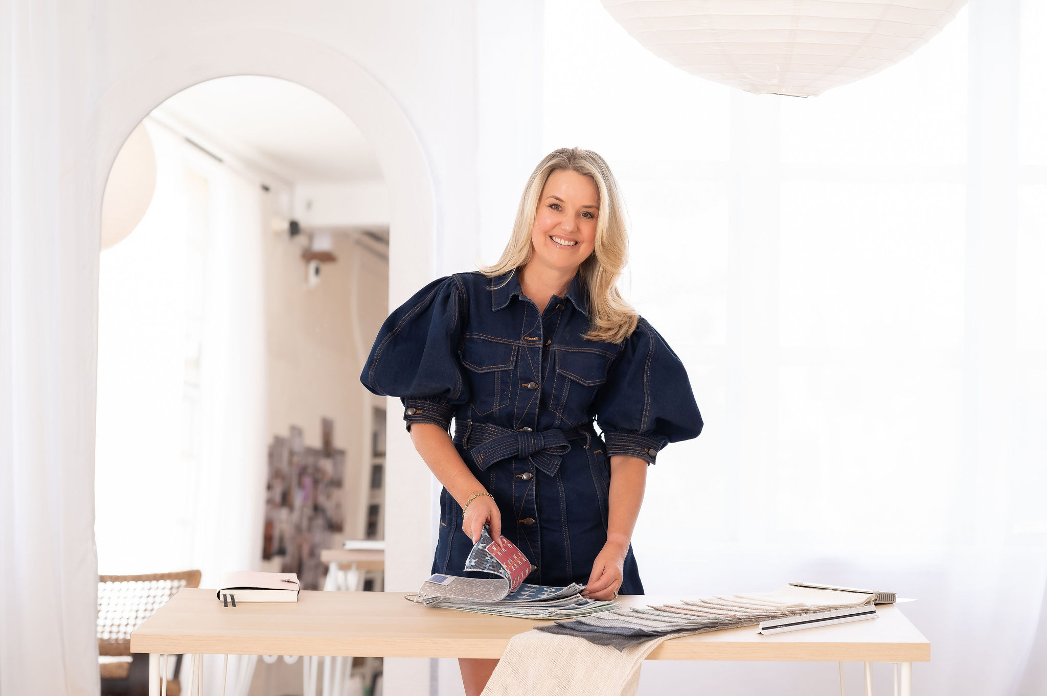 Principal designer at Bella Vie Interiors, Lisa Alward, stands at a work table with fabric samples, embodying professional interior design expertise.