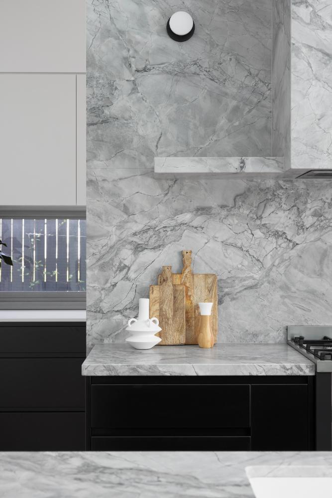 Modern kitchen showcasing striking marble backsplash with contrasting black cabinetry, complemented by wooden cutting boards and white ceramic decor.
