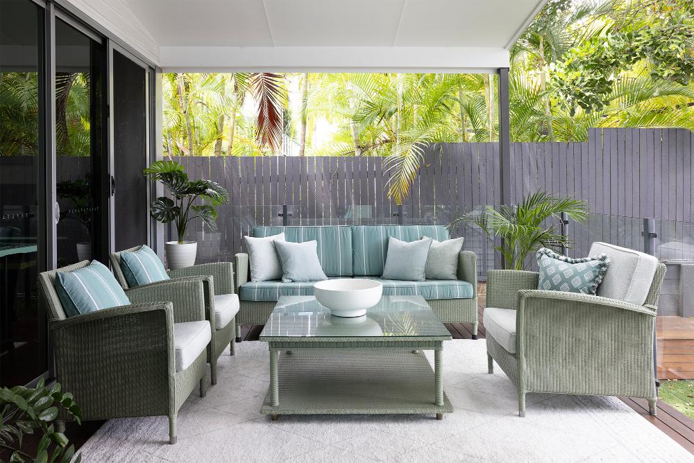 A serene patio area with plush green woven furniture, soft blue cushions, and tropical plants creating a tranquil outdoor retreat.